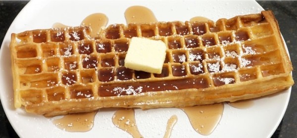 Photo of a keyboard shaped waffle on a plate with sticky syrup, butter, and powdered sugar on top.