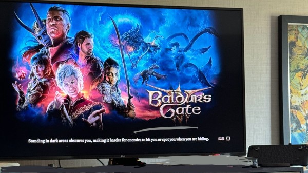 Large Hotel TV showing the Baldur’s Gate 3 loading screen, and off to the size a Steam Deck on a dock