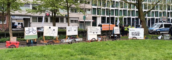 Vor dem Atlantik-Hotel in  Münster steht bei einer Demonstrationen auf der Engelenschanze ein Lastenradanhängergespann mit 5 Lastenanhängern mit Aufstellern zu mehr Platz und Geld für Bahn, Bus, Fuß und Rad.
