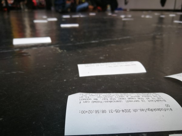Strips of paper strewn across the floor, one is recognizeable as having a toot by infodesk@gulas.ch printed on it.