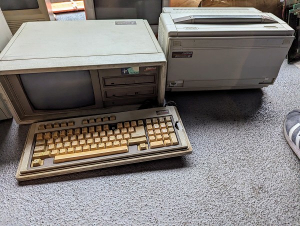 A photograph of two Compaq "luggables" portable computers. The one on the left has the keyboard detached and laying in front of it.  The keys have discolored to a surprisingly attractive orange sherbet shade.  The computer's case is somewhat grimy, and there's a sizable chunk of plastic broken away from the right side of the keyboard.  All the keys are there, though.  A sticker on above the disk drives reads "+ Hardcard."

The computer on the right still has its keyboard covering the monitor and drives, but looks overall to be in slightly better cosmetic shape.  A sticker on the front face -- so, the underside of the keyboard -- reads "Compaq Portable III."