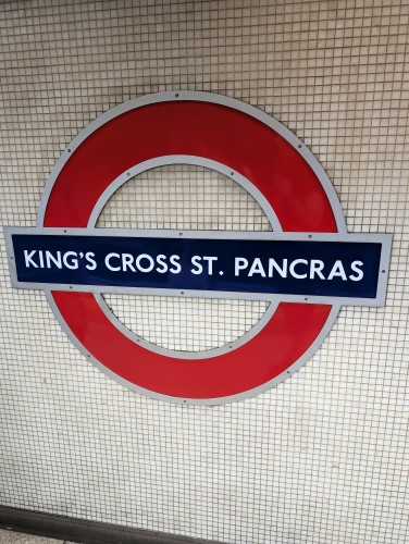 The tube station sign at King's cross - St. Pancras. It's the typical red circle with a dark blue bar with the station name written on top. It's mounted flush on the tiled wall.