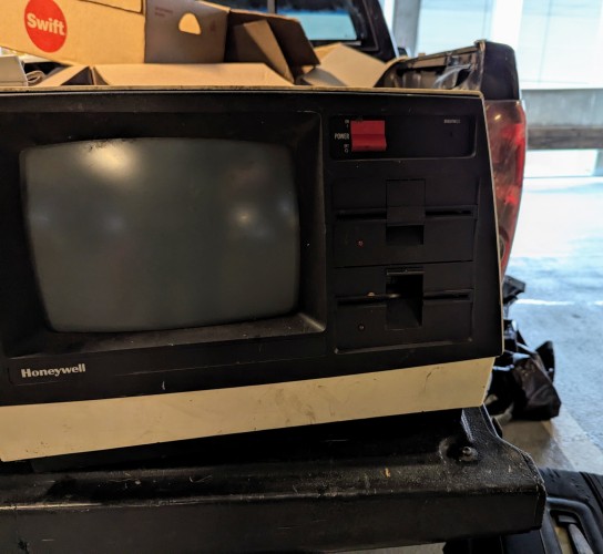 A photograph of a Honeywell personal computer, black face set in a beige box.  A distinctly convex CRT monitor is set into the left side, above the Honeywell name.  To the right of that, vertically from top to bottom in the black face, are a very chunky red power switch and a brightness dial, then two 5¼ floppy drives.