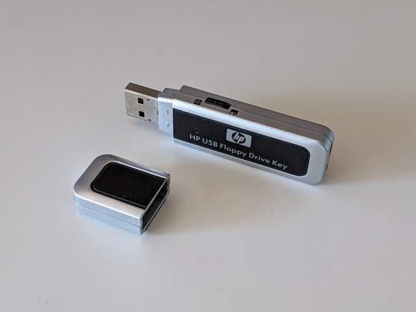 A photo of a HP USB Floppy Drive Key, a strange USB flash drive with a slide switch on top labeled with CD and floppy disk icons.