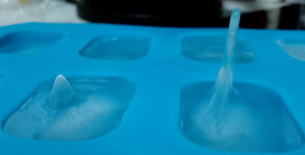 A blue ice cube tray, with a tall spike sticking out of one ice cube and a smaller bump in the cube next to it.