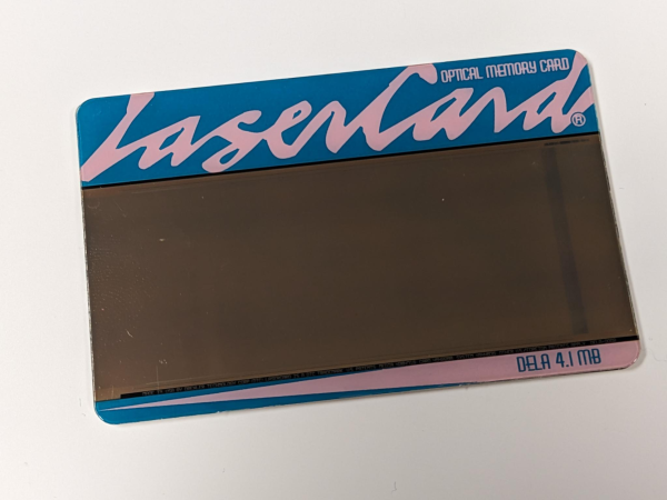 credit card sized card in turquoise with pink script reading LaserCard and smaller text reading Optical Memory Card, DELA 4.1 MB, with a large silvery data section in the middle