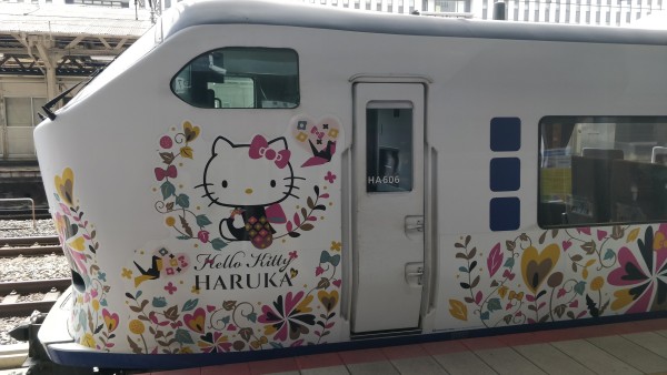 Outside photo of a white train standing at a platform of a train station with colorful flower ornaments design and a Hello Kitty Figure wearing a Kimono.