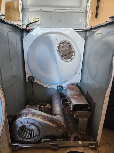 The inside of a dryer, missing the drum and some front cover components. It's very linty. 