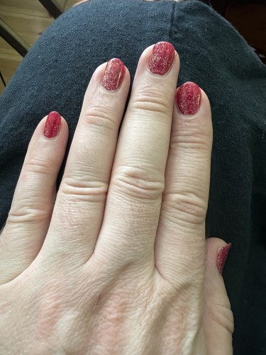 My left hand with dark red painted nails with a layer of silver glitter on top