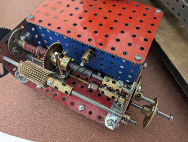 A Meccano contraption with brass gears, springs, and a threaded rod. All arranged to hold a plastic tube in position for a rotating cutter to come in at a right-angle and mill a thread.