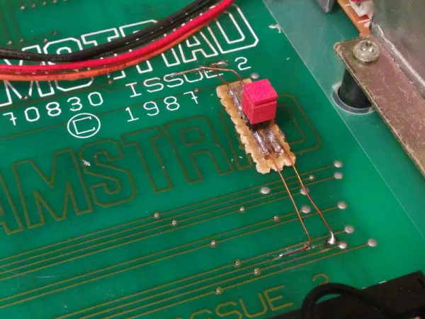 Two removable jumpers soldered to a small scrap of prototyping board, which is itself glued onto a large green PCB. Four very thin wires bridge signals between the two boards