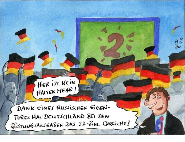 Die Karikatur zeigt eine Menschenmenge vor einer Leinwand auf der eine 2 auf dem Rasen prangt. Es wehen Deutschlandflaggen und Hüte fliegen durch die Luft. Im Vodergrund steht ein Reporter, der sagt: „Hier ist kein Halten mehr! Dank eines russischen Eigentores hat Deutschland bei den Rüstungsausgaben das 2%-Ziel erreicht!"