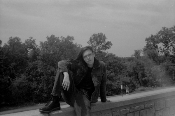 A black and white film photo of me posing on a brick wall, I look cool as fuck