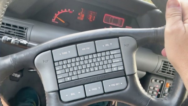 A picture of the steering wheel from a Pontiac Grand Prix, covered in numerous buttons including a full qwerty keyboard.