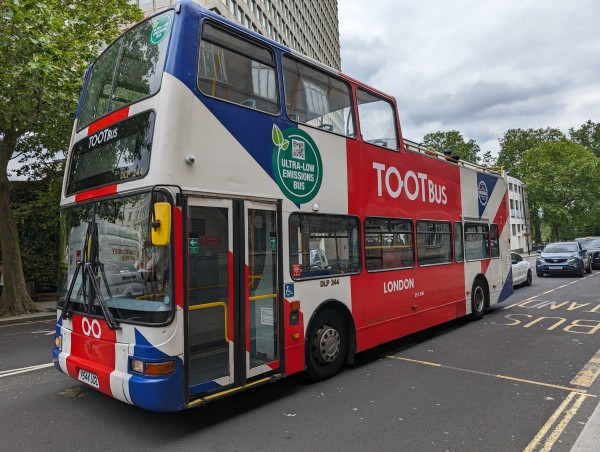 A typical London double decker bus with a union jack all over it and part of the roof missing. On the side it says "TOOT Bus". 
