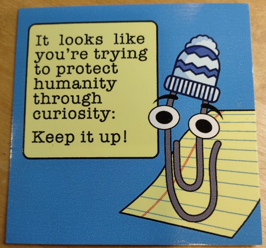 Clippy wearing a striped beanie hat with text "It looks like you're trying to protect humanity through curiosity: Keep it up!"