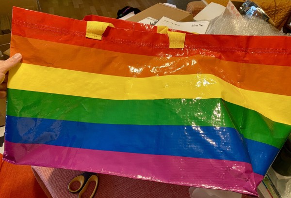 A large bag made of woven plastic. It’s in the colors of the rainbow Pride flag. 