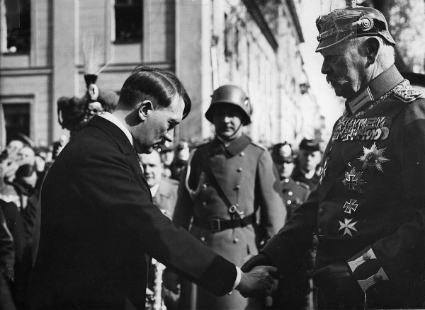 Schwarz-weiß Foto von Adolf Hitler, der dem Reichspräsidenten Hindenburg die Hand gibt und den Kopf senkt.