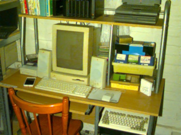 A photo of a desk in the style of 1994, and the photo itself is in the style of 1994. Yellowed highlights, bad resolution, flash, and generally a fuzzy awful look to it. There is a modern iPhone on the desk.