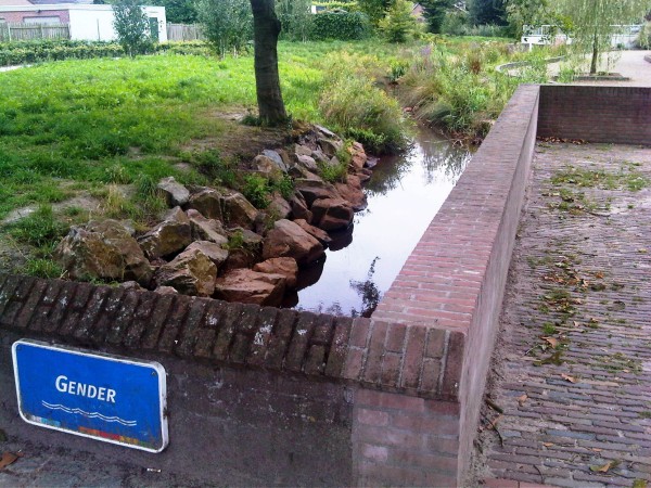 A small stream passing under a bridge, on which there's a small sign which proudly proclaims its name, which is simply "Gender".
