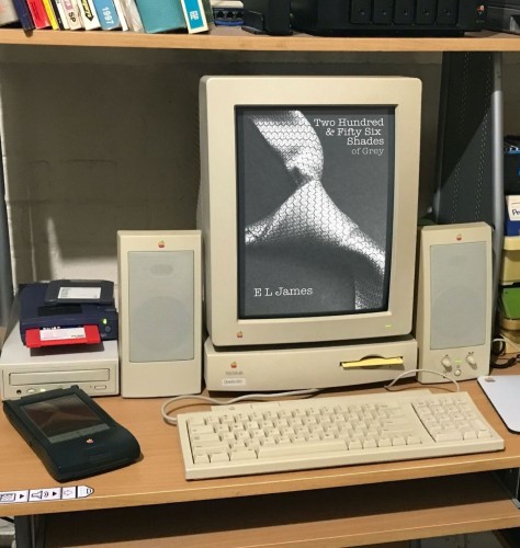 A photo of a desk with a Macintosh Quadra setup and a 256 greyscale portrait display showing the cover of the book Two Hundred & Fifty Six Shades of Grey by E L James. Also the Newton on the desk is displaying the cover of the abridged version, Sixteen Shades of Grey.